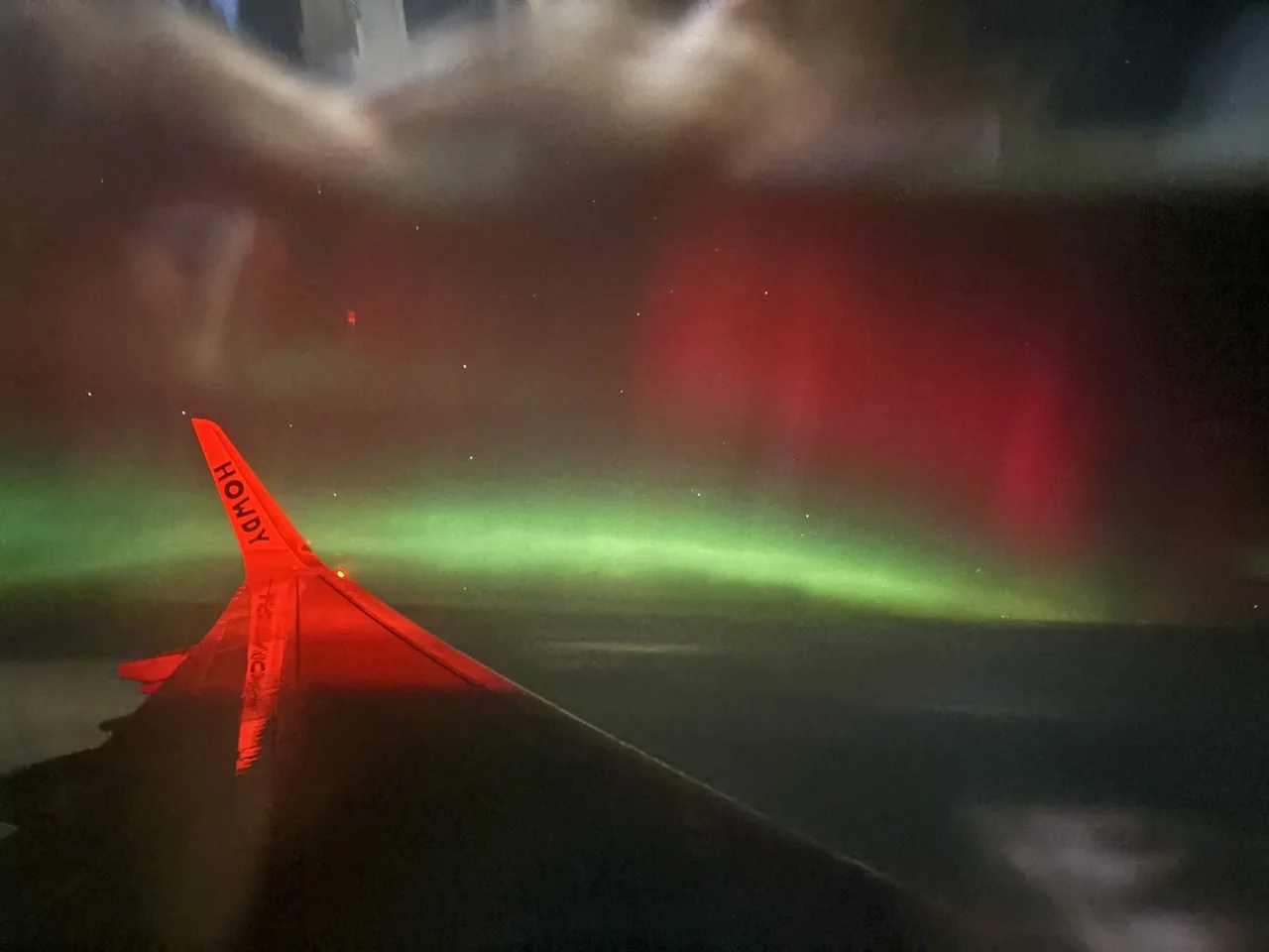 Green and red aurora visible beyond an airplane wing at night
