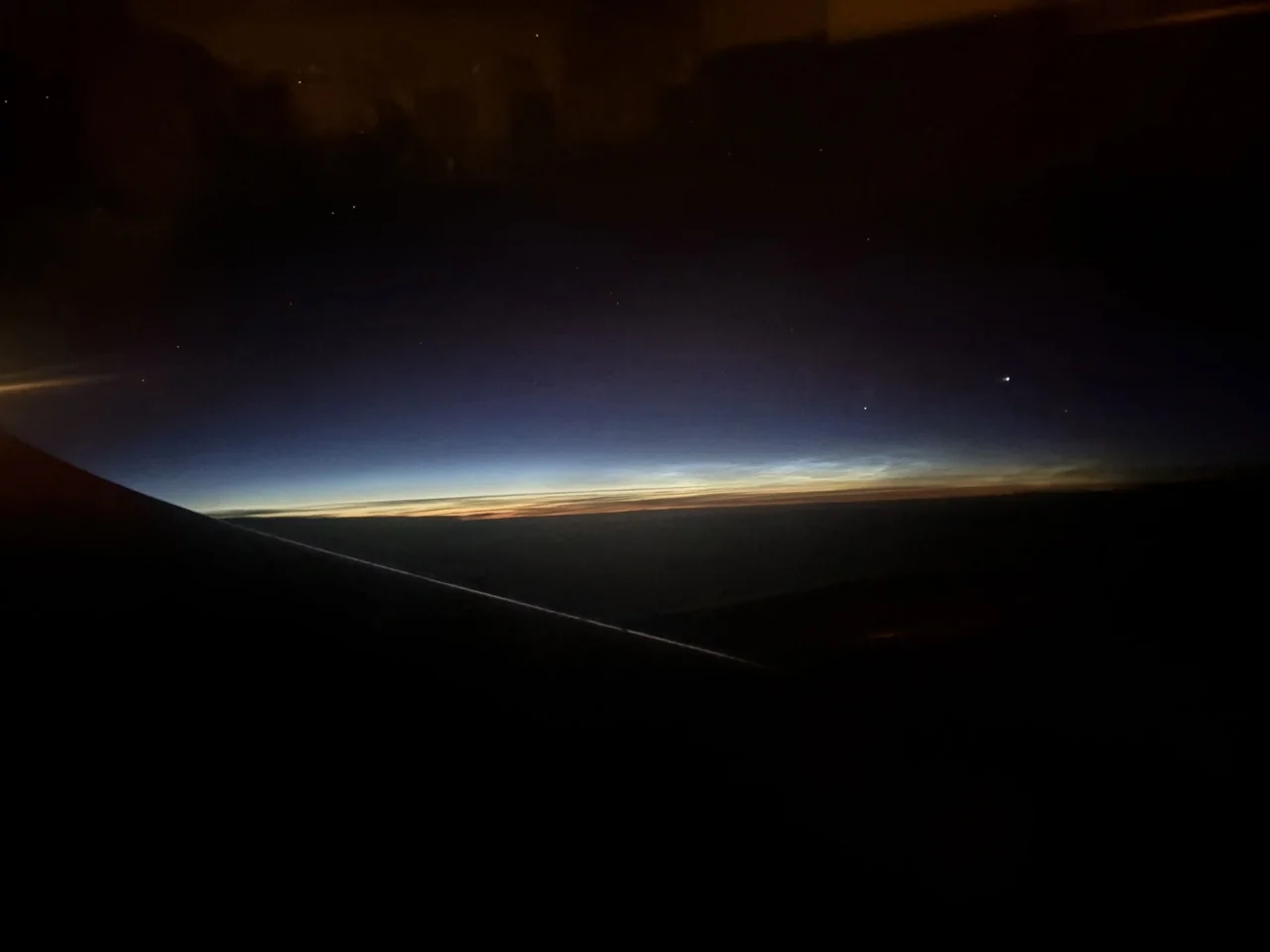 A dark airplane wing beneath a thin twilight horizon and stars