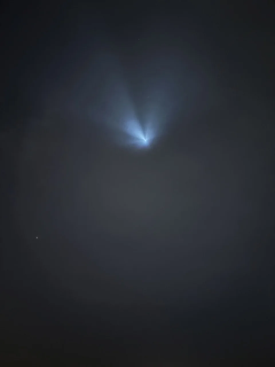 A blue-white luminous plume spreading through a dark cloudy sky