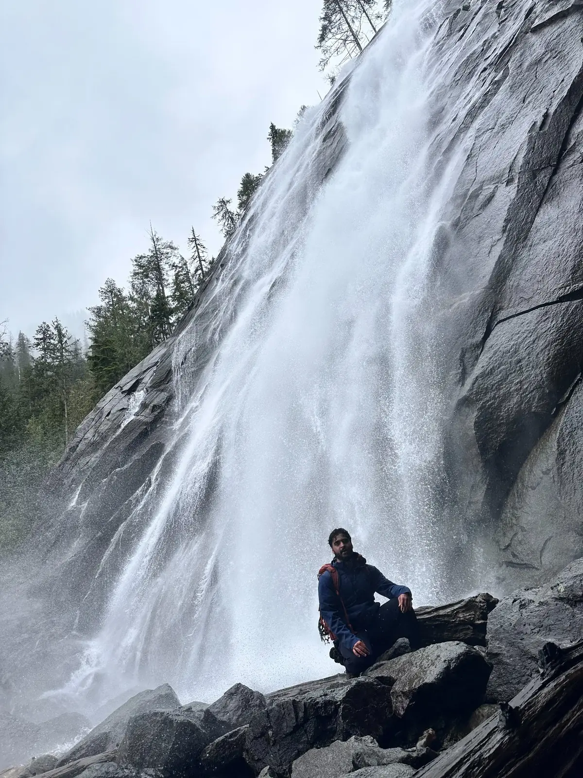 Waleed seated on rocks beside a large mountain waterfall