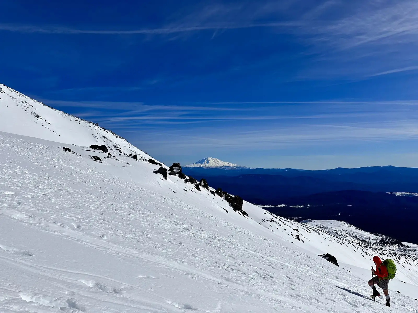A climber crossing a broad snowy slope with a distant volcano on the horizon