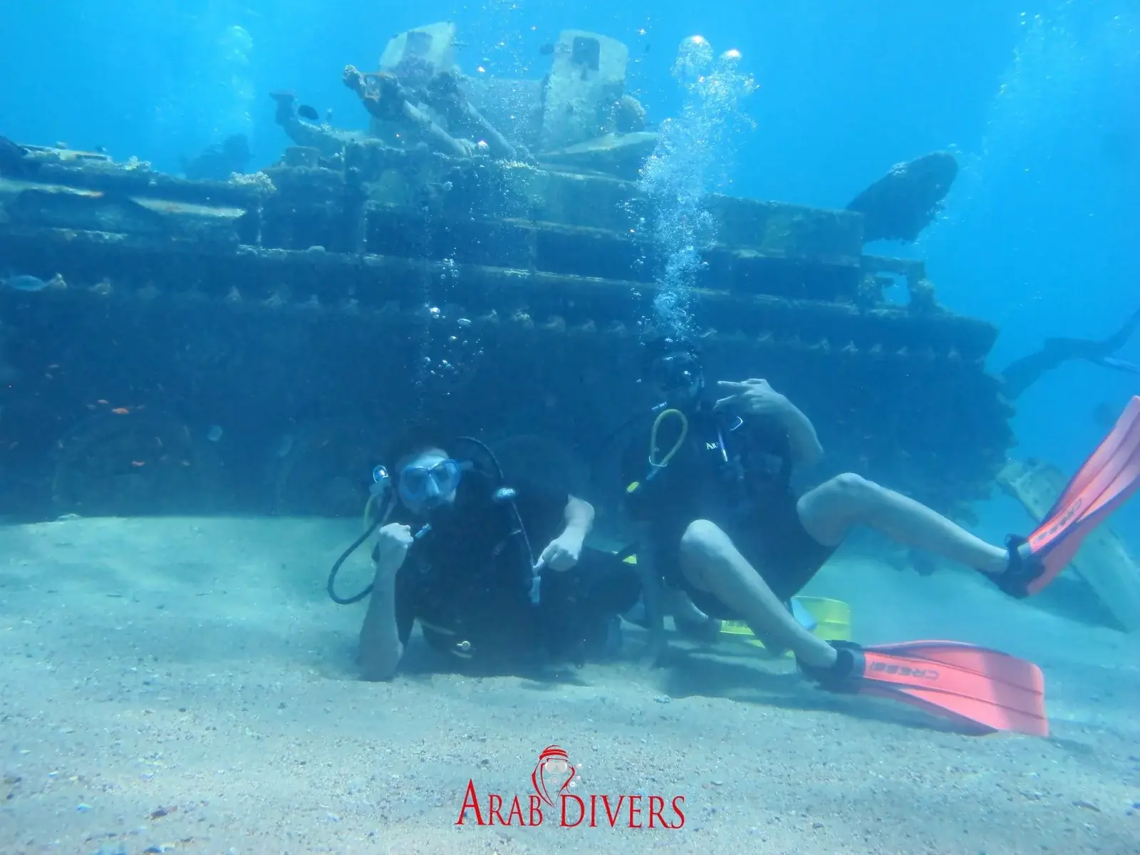 Two scuba divers resting on the seafloor beside a submerged wreck