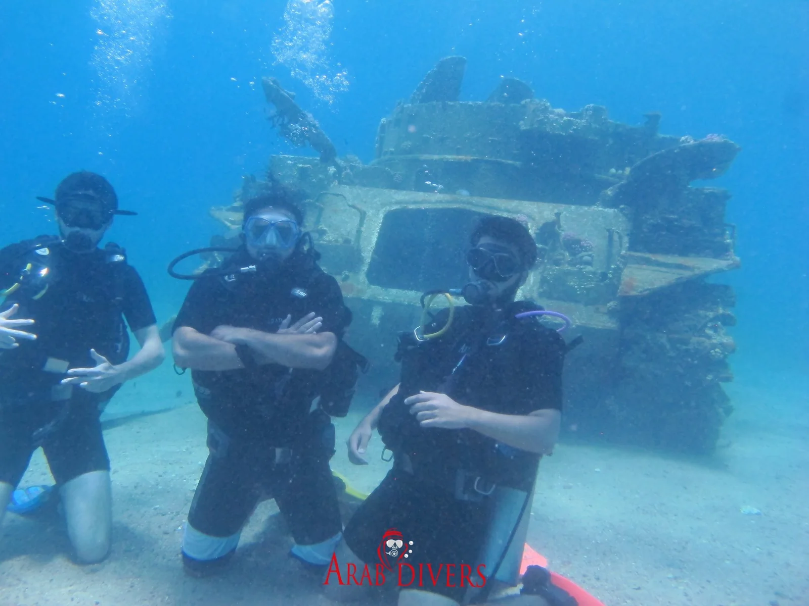Three scuba divers positioned in front of a submerged military wreck in the Red Sea