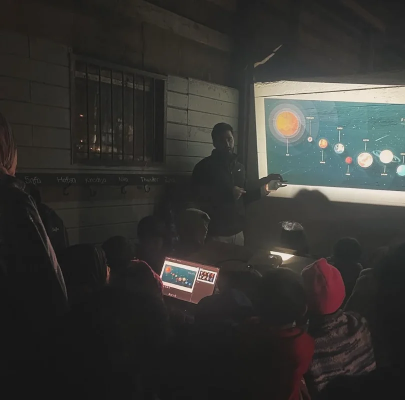 Waleed presenting a projected solar system diagram to children at night