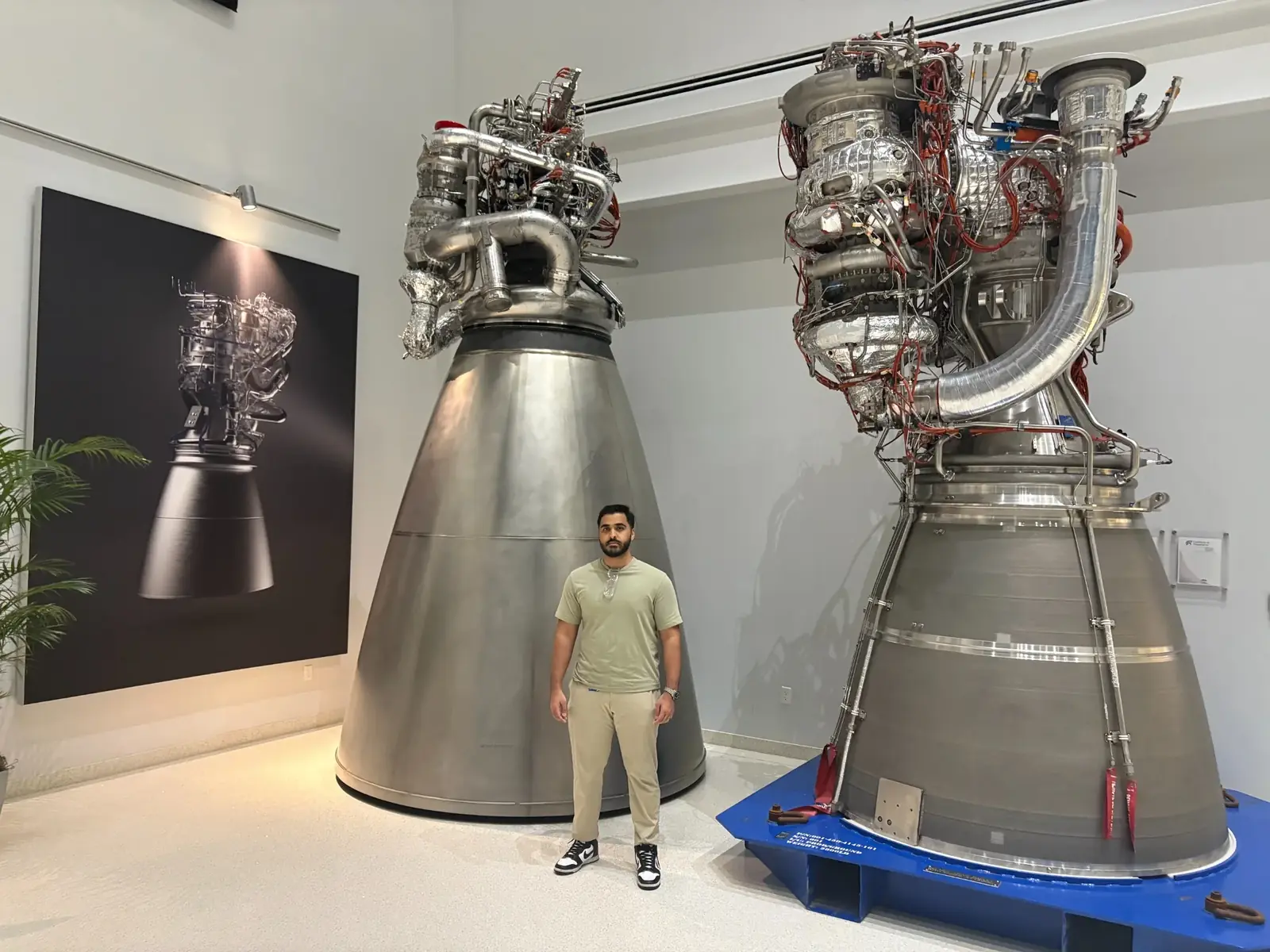 Waleed standing between two large rocket engines in a Blue Origin display area